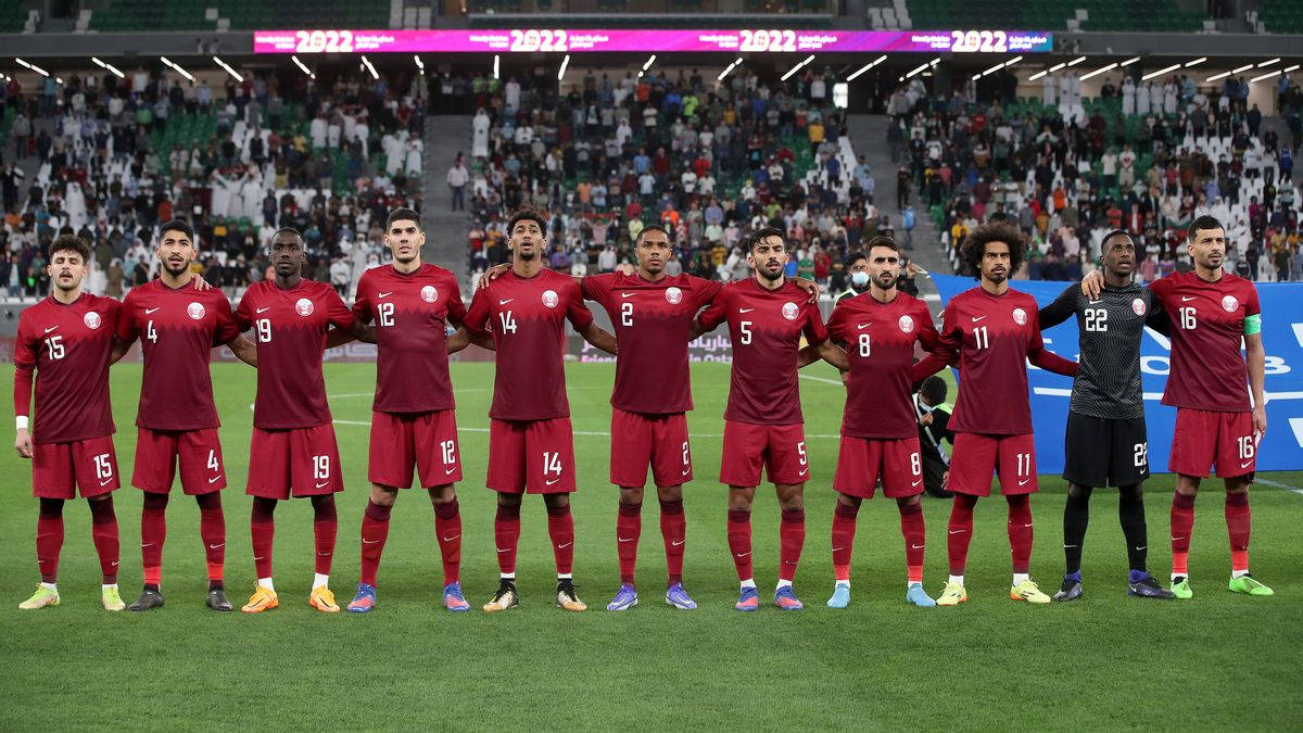 Qatar 桌布 壁紙 — 卡塔爾國家足球隊球員身穿紅色球衣，在球場燈光下於綠色草地上排成一列，背景有球迷。