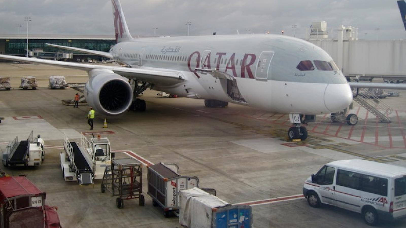 卡塔爾航空飛機在機場閘口，有地勤人員和服務車輛。