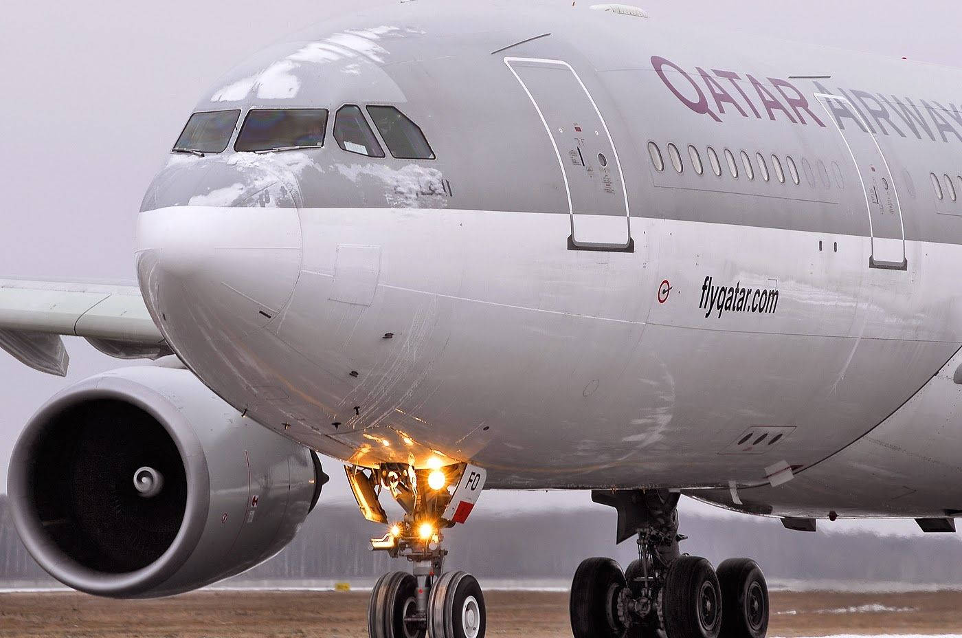 卡塔爾航空飛機在積雪跑道上，起落架燈閃爍。