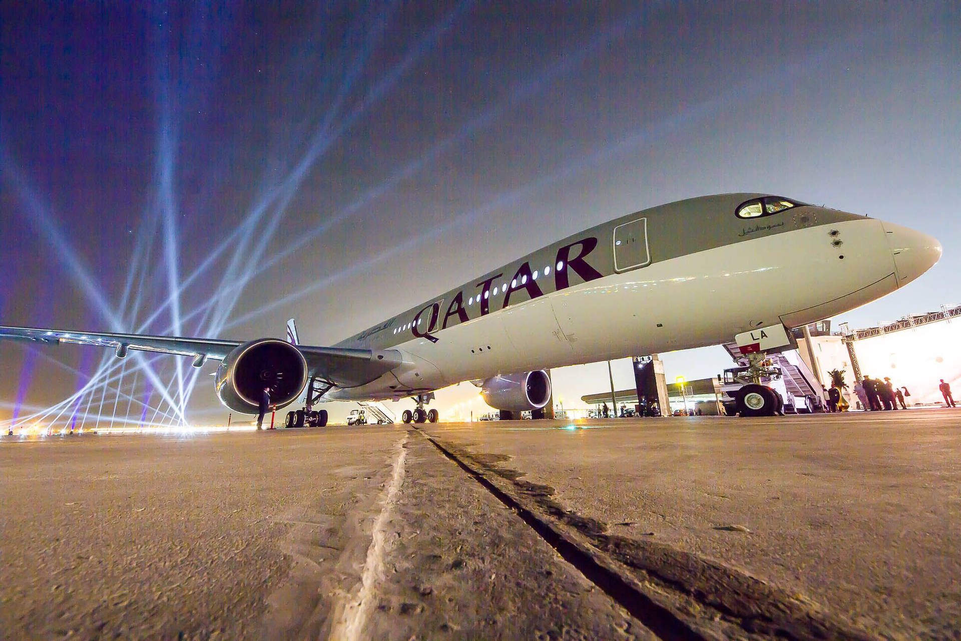 一架卡塔爾航空飛機在夜間機場停機坪上被藍色聚光燈照亮。