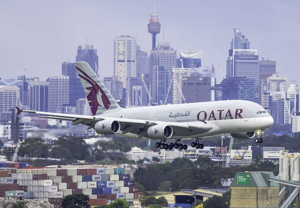 卡塔爾航空A380飛機在港口附近降落，背景為城市天際線