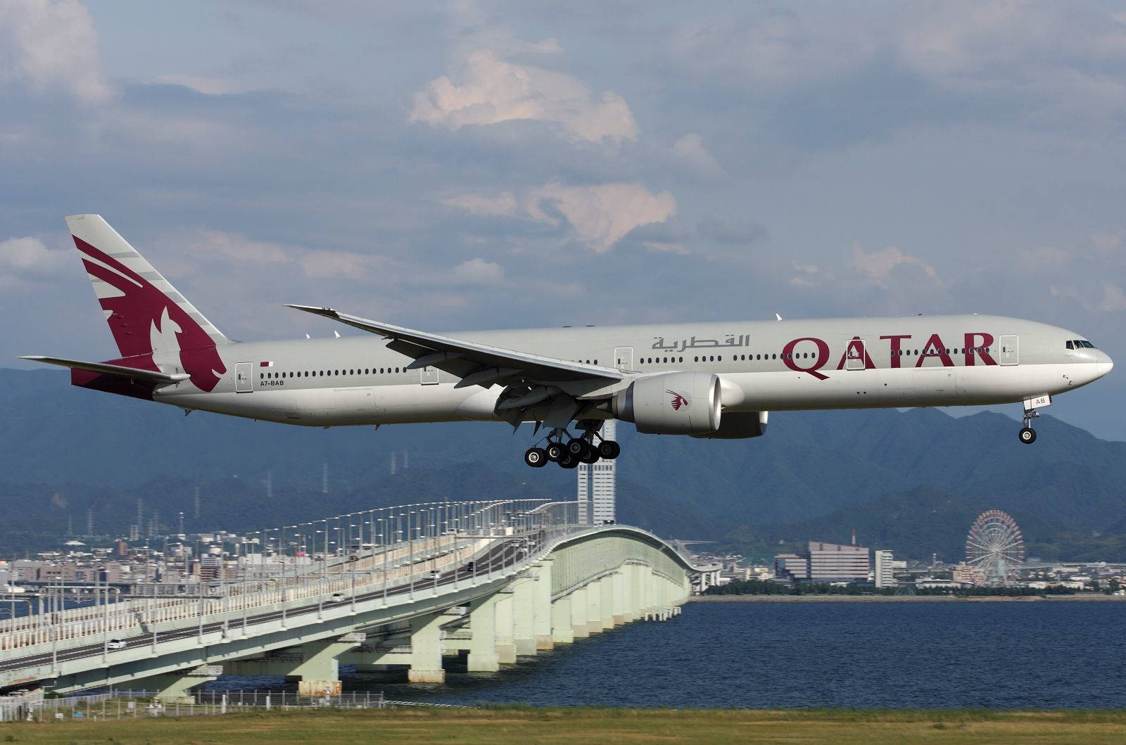 卡塔爾航空飛機在靠近城市有摩天輪的橋樑上空起飛。