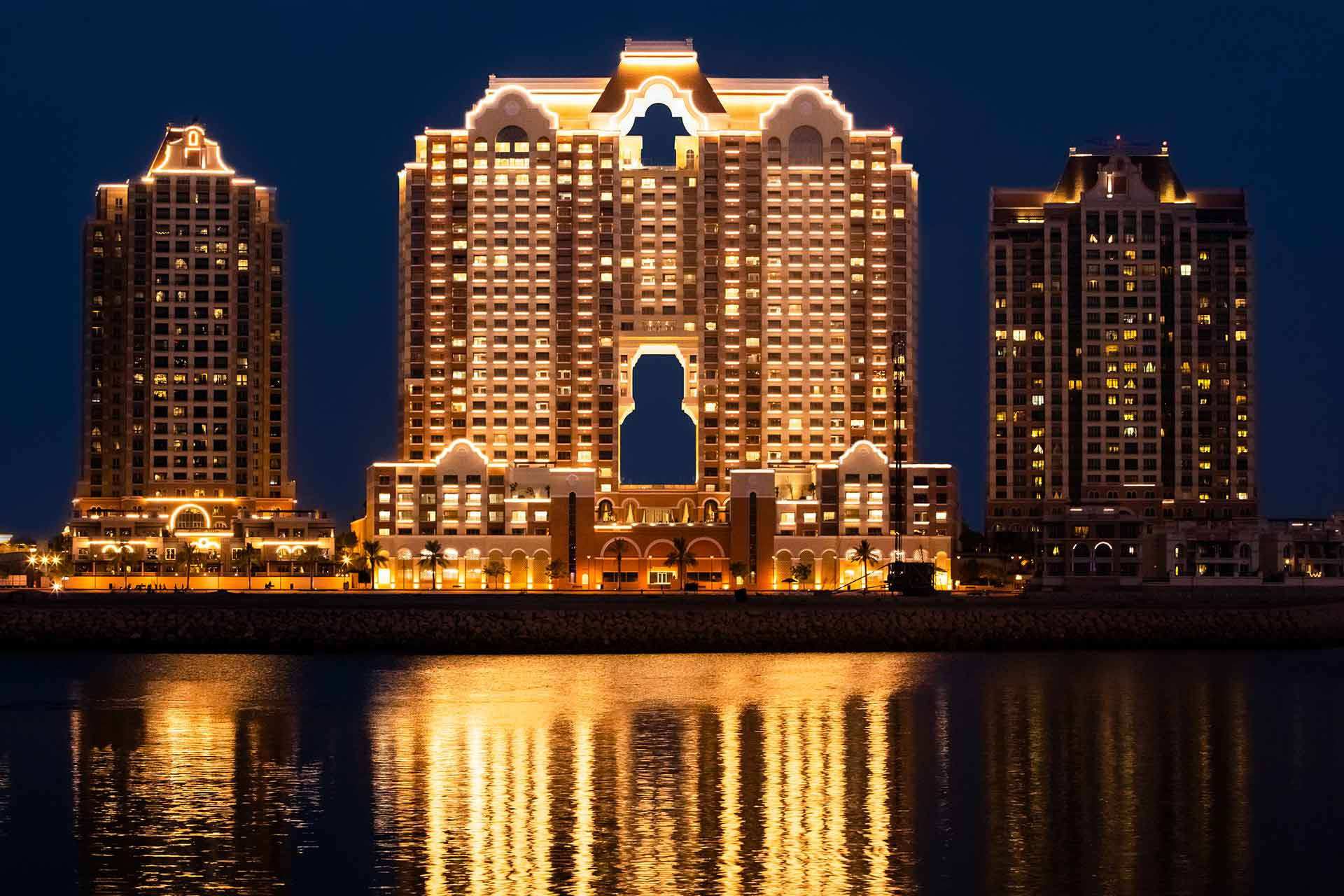 卡塔爾阿穆塔希德大樓 壁紙 — 在深邃的夜空下，宏偉的燈光酒店塔樓溫暖地倒映在平靜的水面上。