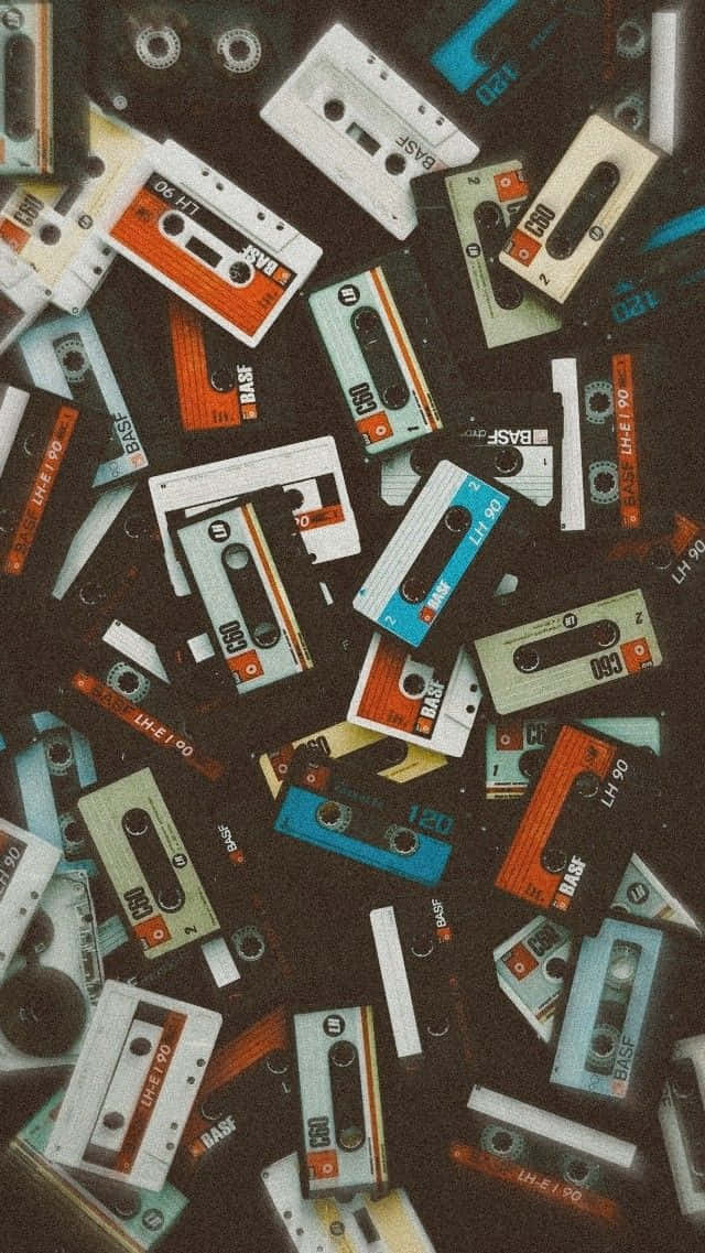 卡式錄音帶復古90年代背景 壁紙 — 一堆散落的復古錄音卡式帶，顏色和品牌各異，背景為深色紋理。