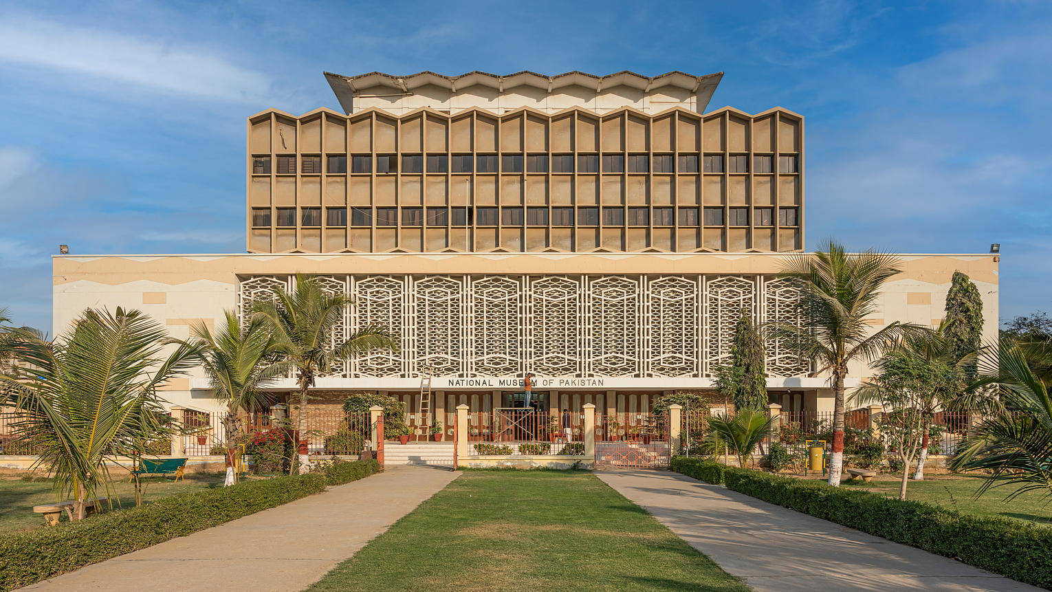 卡拉奇巴基斯坦國家博物館 壁紙 — 大型米色巴基斯坦國家博物館矗立在晴朗藍天下，棕櫚樹和修剪整齊的草坪環繞著中央步道。