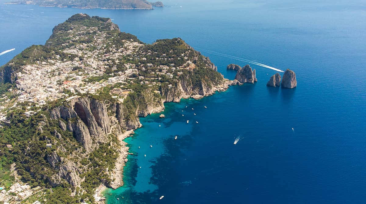 Italian Island 桌布 壁紙 — 卡普里島的鳥瞰圖，碧綠海水、船隻和陽光下標誌性的法拉廖尼岩石。