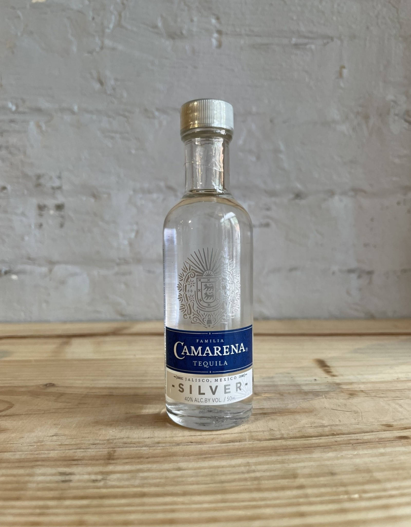 卡曼納銀色龍舌蘭酒 40% 酒精度 壁紙 — 一瓶透明的 Camarena Silver 龍舌蘭酒放在淺色木質表面上，背景是帶紋理的白色磚牆。