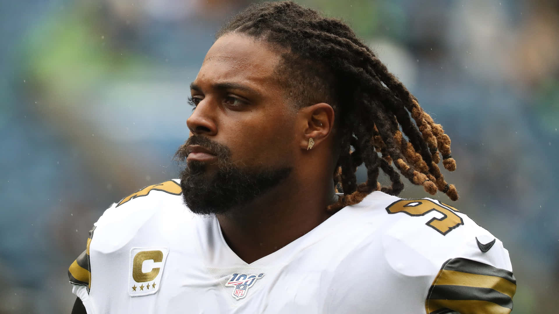 NFL美式足球員在雨中穿著帶有隊長臂章的白金色制服。