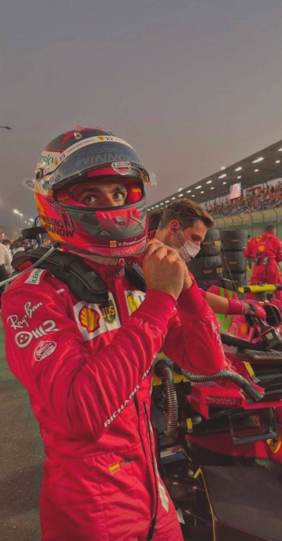 身穿紅色賽車服的F1車手在黃昏的賽道上調整頭盔。