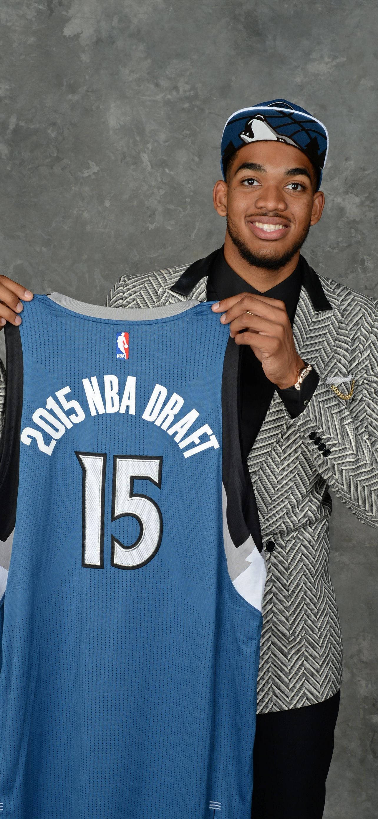卡爾-安東尼·唐斯 NBA 選秀 壁紙 — 一位微笑的年輕籃球運動員自豪地舉起他的2015年NBA選秀球衣15號，背景是灰色攝影棚。