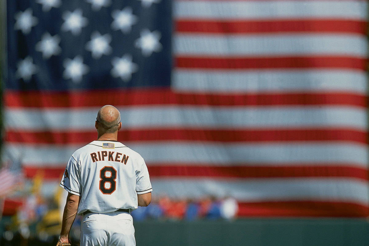 卡爾·里普肯背對美國國旗 壁紙 — 一位光頭棒球運動員穿著Ripken 8球衣，背對鏡頭，面向一面大型模糊的美國國旗。