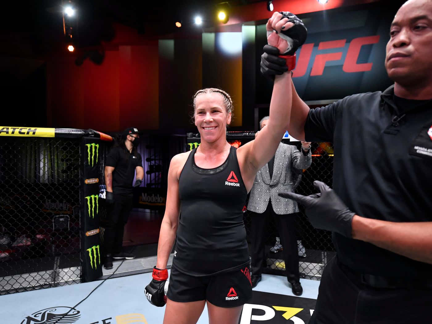 卡特琳·丘卡吉安獲勝慶祝 壁紙 — 一位勝利的女性MMA拳手在明亮的場館燈光下，於UFC八角籠內被裁判舉起手時微笑。