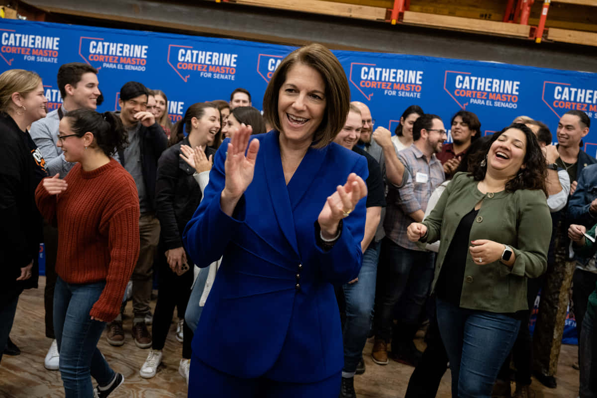 卡特琳娜·科爾特斯·馬斯托官方攝影 壁紙 — Catherine Cortez Masto 在一個充滿活力的藍色背景的競選活動中，熱情地向支持者揮手。