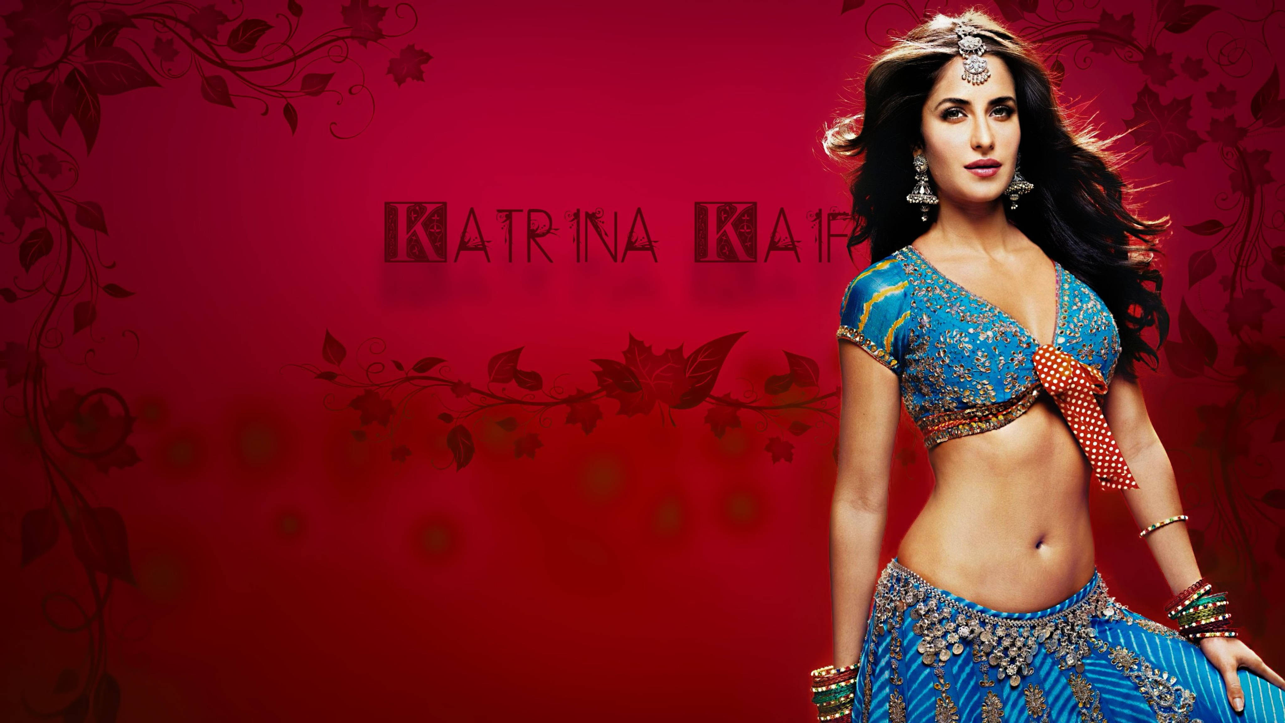 卡特里娜·凱芙印度寶萊塢女星 壁紙 — Katrina Kaif 自信地擺姿勢，身穿藍色裝飾的 lehenga，背景是帶有花卉圖案的濃郁紅色。