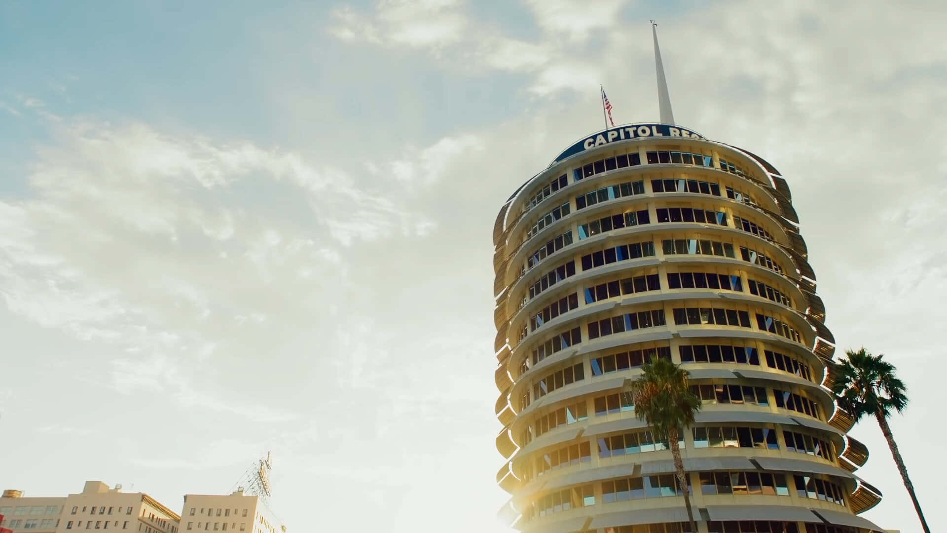 卡皮托爾唱片大樓的地面視角 壁紙 — 以低角度觀看標誌性的 Capitol Records 大樓，沐浴在金色夕陽中，棕櫚樹環繞其螺旋結構。