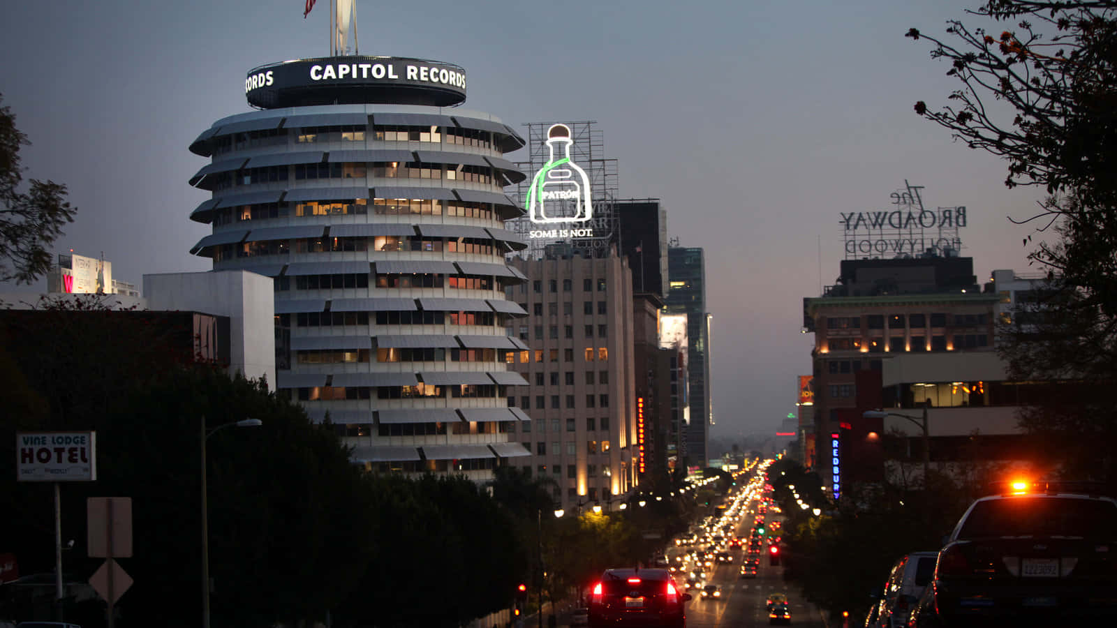 卡皮托爾唱片大樓與街燈的視角 壁紙 — 荷里活的黃昏，Capitol Records 大樓亮起燈光，車流沿著一條佈滿標誌性招牌的繁華街道流動。