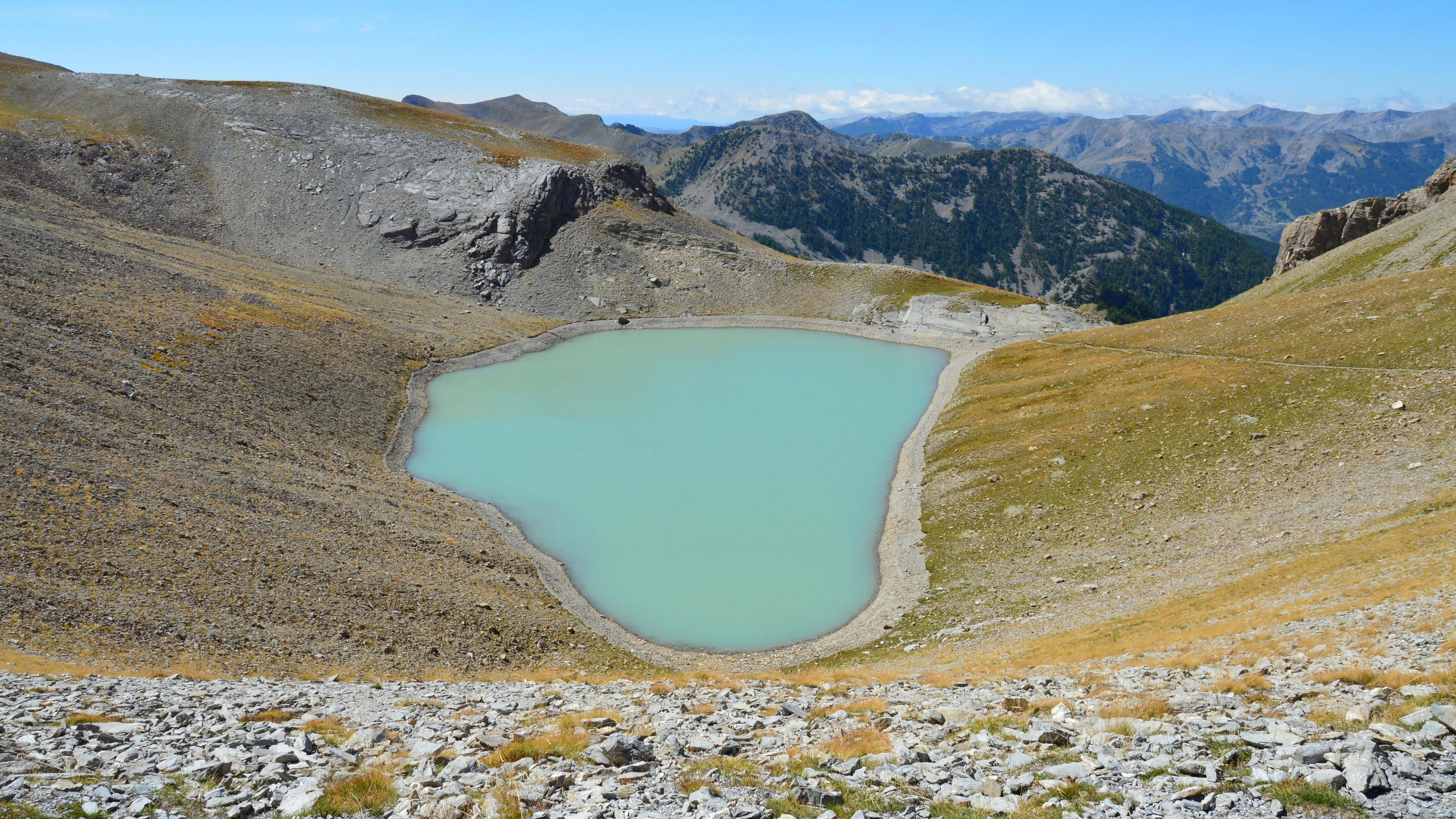 卡約勒小湖 壁紙 — 一個碧綠色的山間湖泊，坐落在岩石山谷中，在晴朗的藍天下，遠處有山峰。