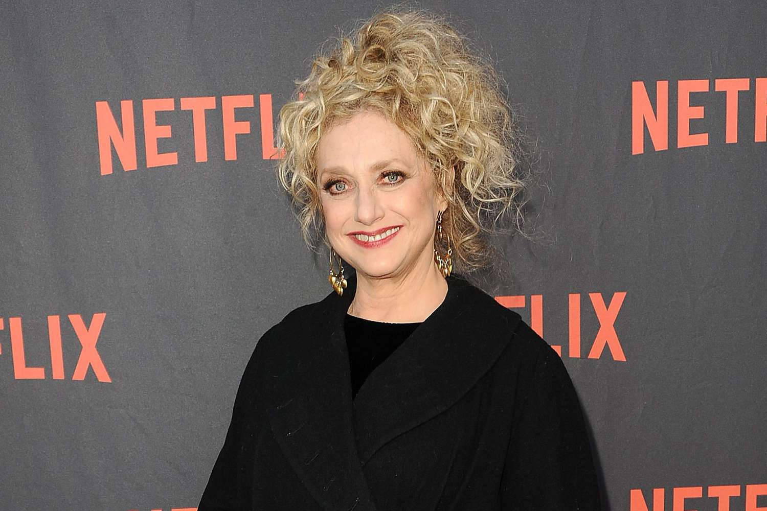 在Netflix活動中，身穿黑色外套的女性對著鏡頭微笑。