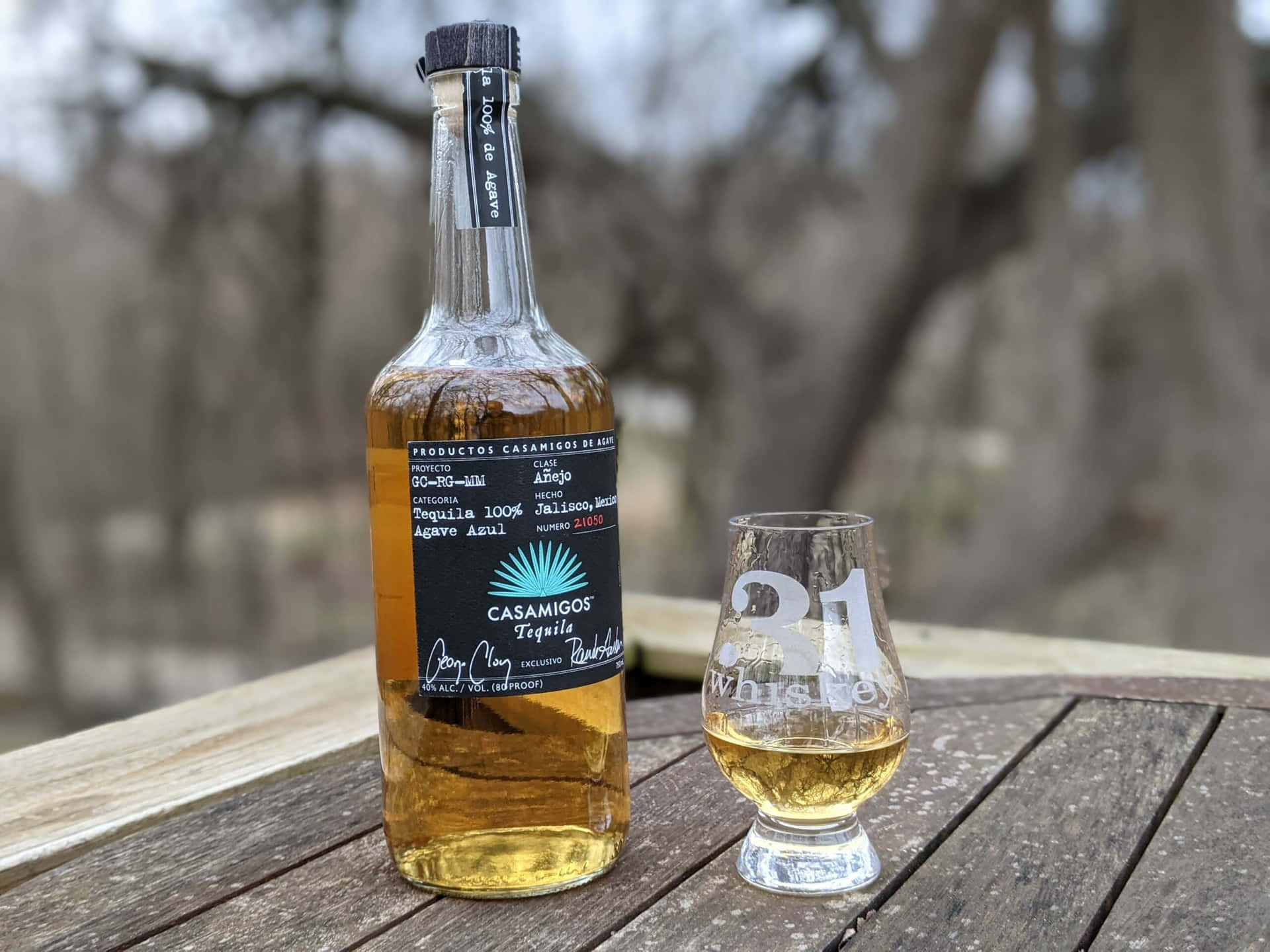 一瓶Casamigos tequila和一個品牌玻璃杯放在戶外的木桌上。
