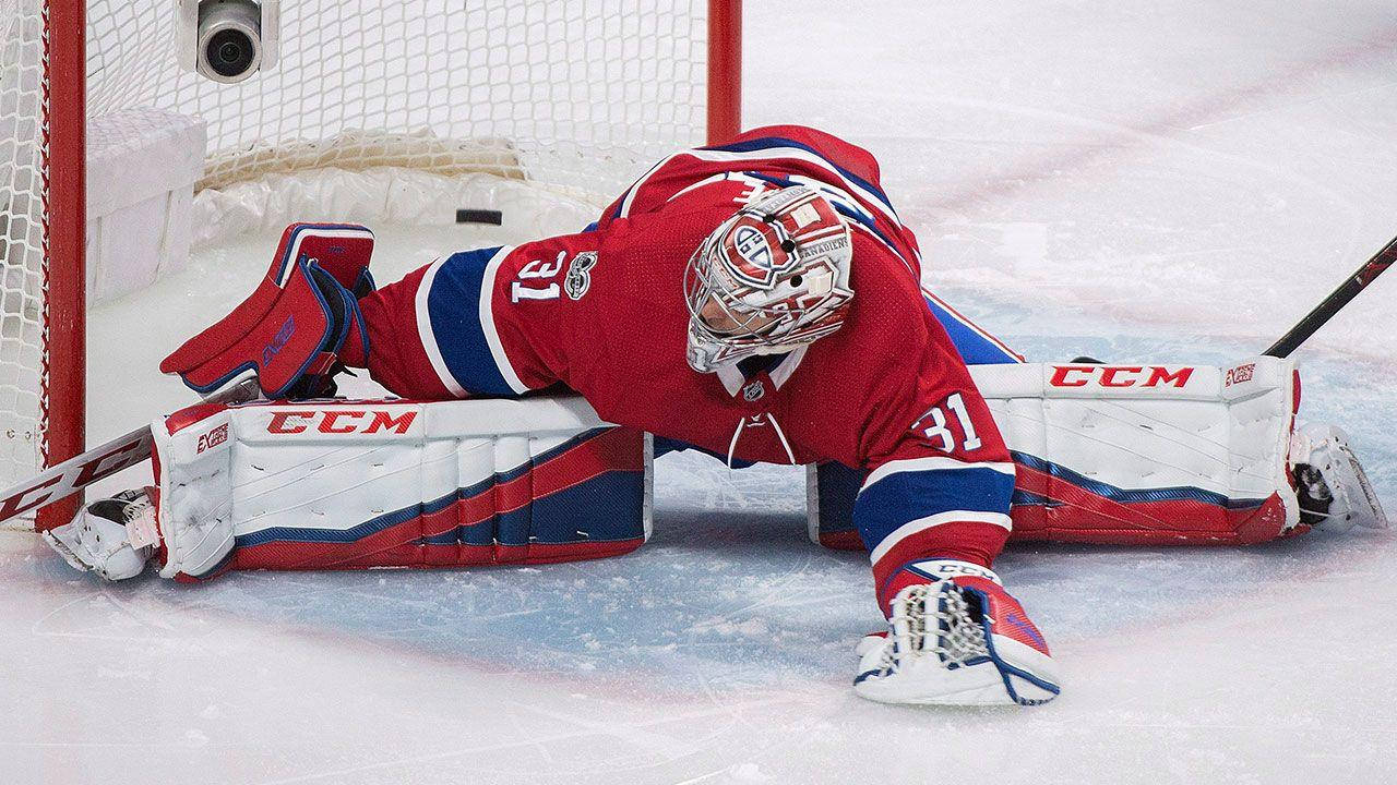 卡里·普萊斯 冰球 NHL 門將 擋球攝影 壁紙 — 一名身穿紅、藍、白色裝備的冰球守門員在冰上飛撲，試圖擋下球門附近的射門。