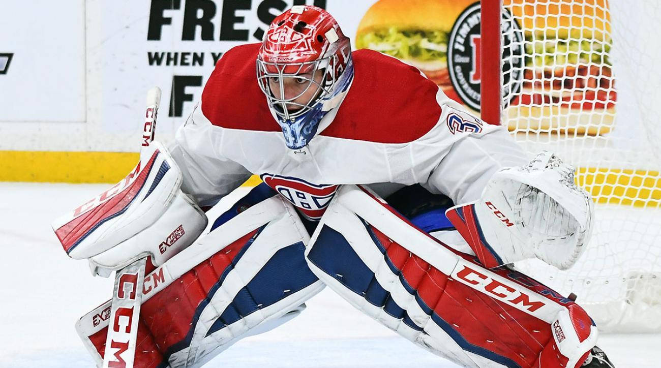 卡里·普萊斯NHL冰球門將攝影 壁紙 — 一名身穿紅白藍裝備的冰球守門員在冰上低蹲，準備在球門附近擋住射門。