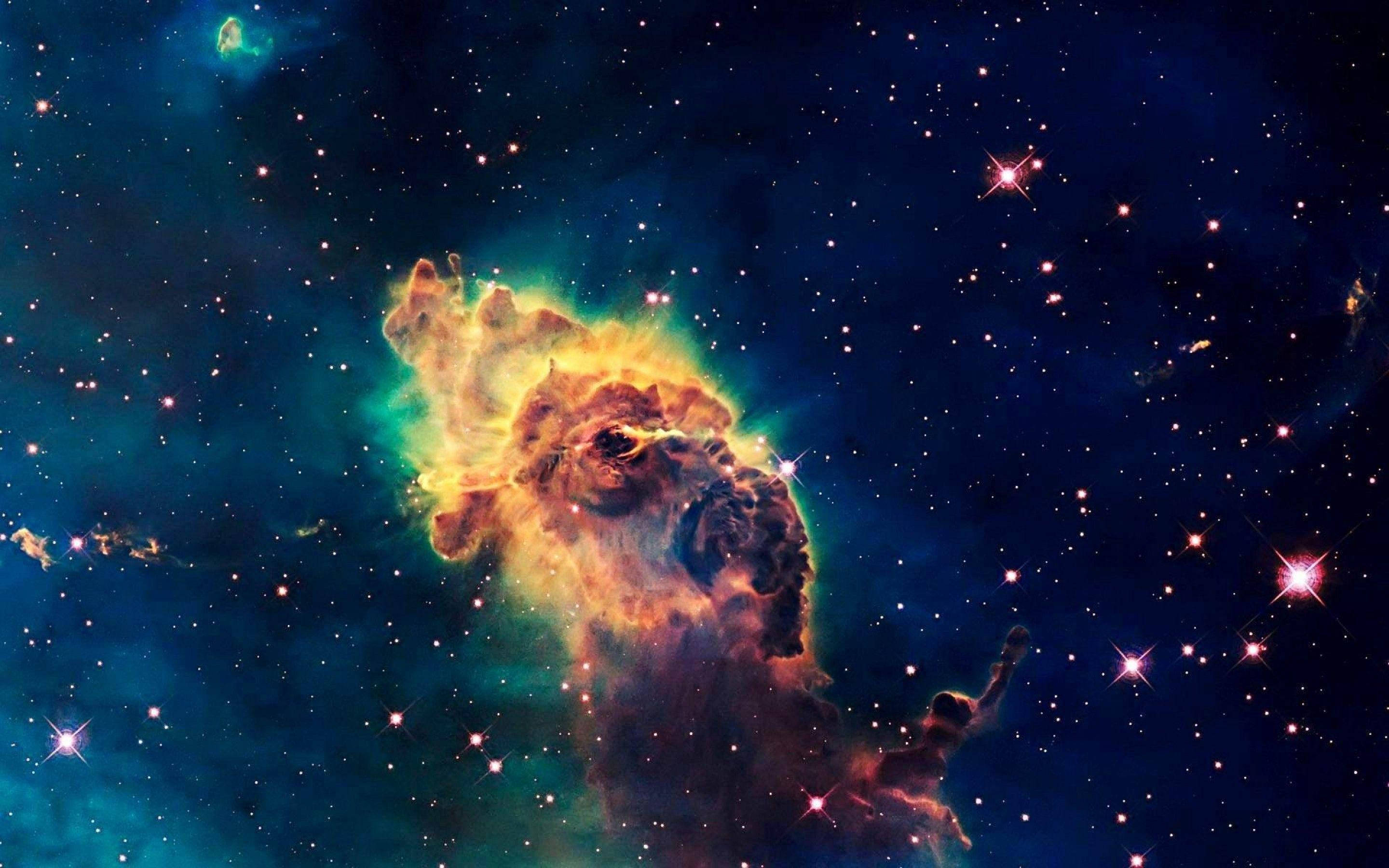 卡里納座藍色星系噴流 壁紙 — 一個充滿活力的宇宙星雲，在深空中閃爍的星場背景下，散發著火橙色和藍綠色的光芒。