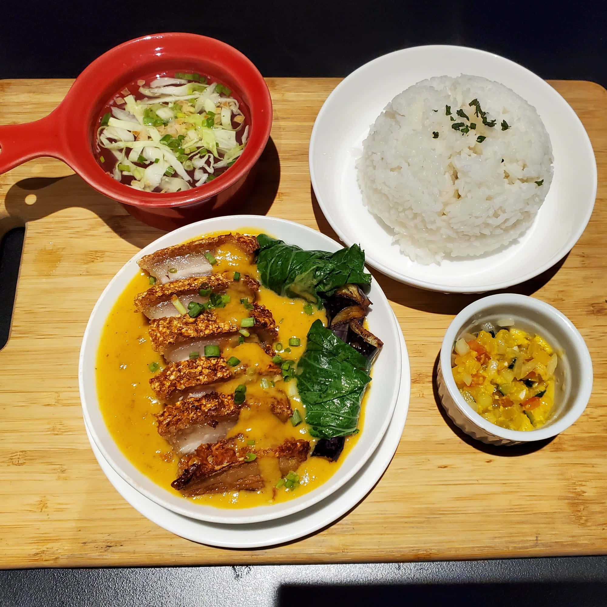 卡雷卡雷配白飯與配菜 壁紙 — 一個充滿活力的餐點，包括脆皮豬肉配黃色醬汁、米飯和配菜，放在木板上。