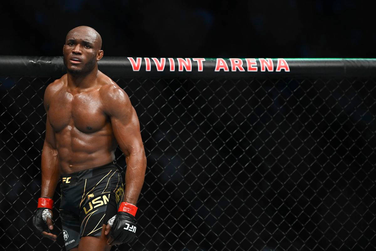 一名赤裸上身的MMA戰士，穿著黑色短褲和手套，站在Vivint Arena的籠子裡。