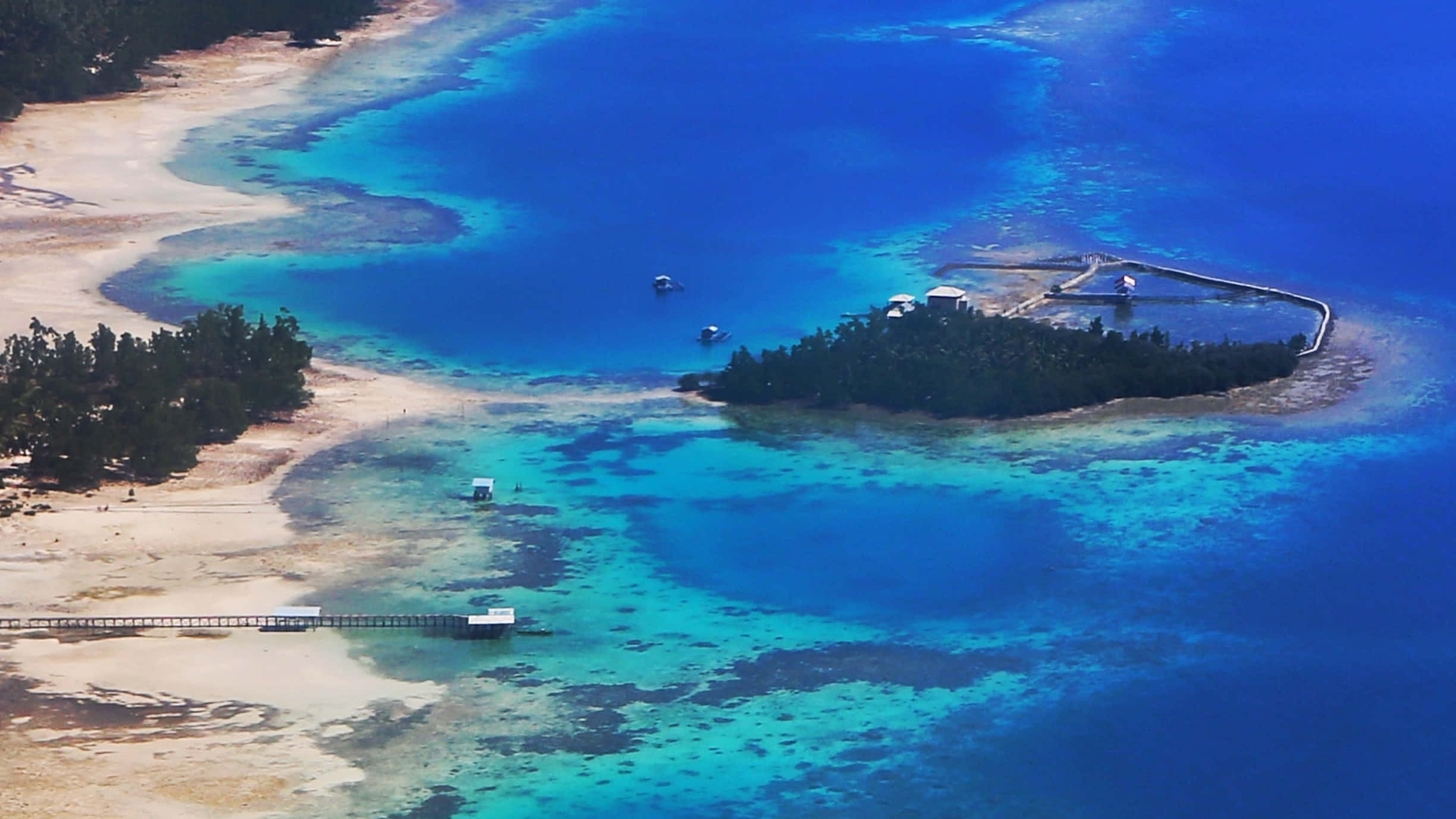印尼蘇拉威西阿曼帕納鎮的壯麗風景 壁紙 — 熱帶島嶼的鳥瞰圖，擁有碧綠色的潟湖、珊瑚礁和延伸到深藍色海洋的木製碼頭。