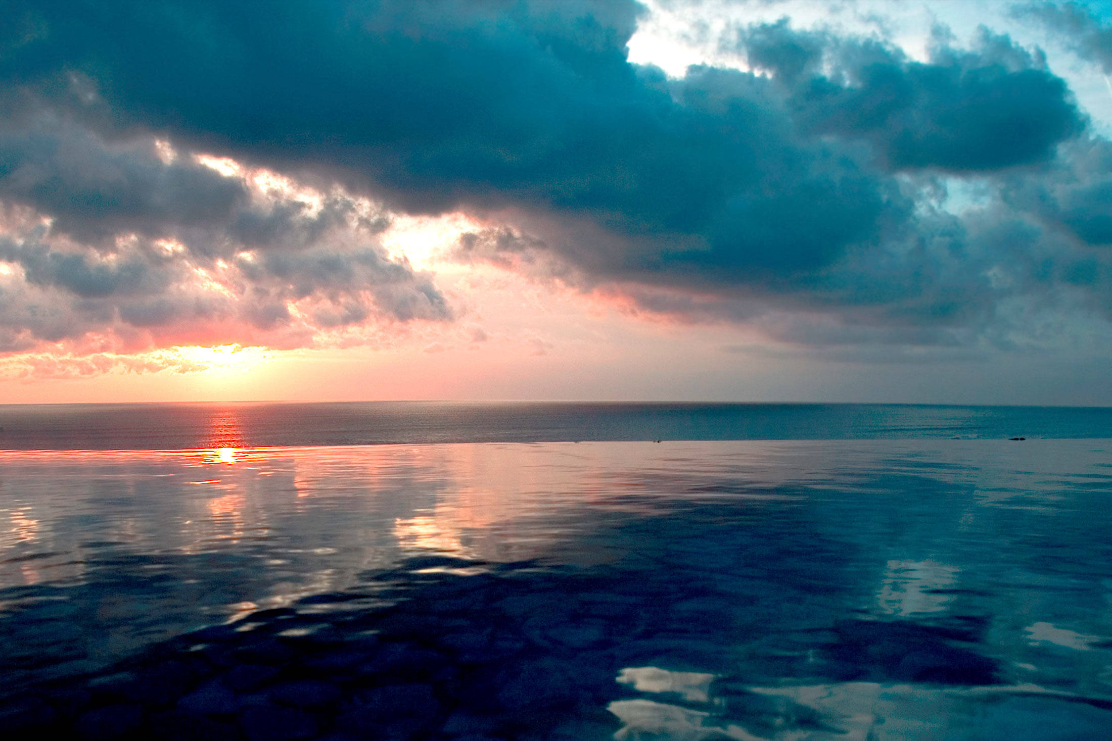 印尼開闊海洋 壁紙 — 夕陽將天空染成火橙色和深青色的雲彩，映照在平靜的海面上。