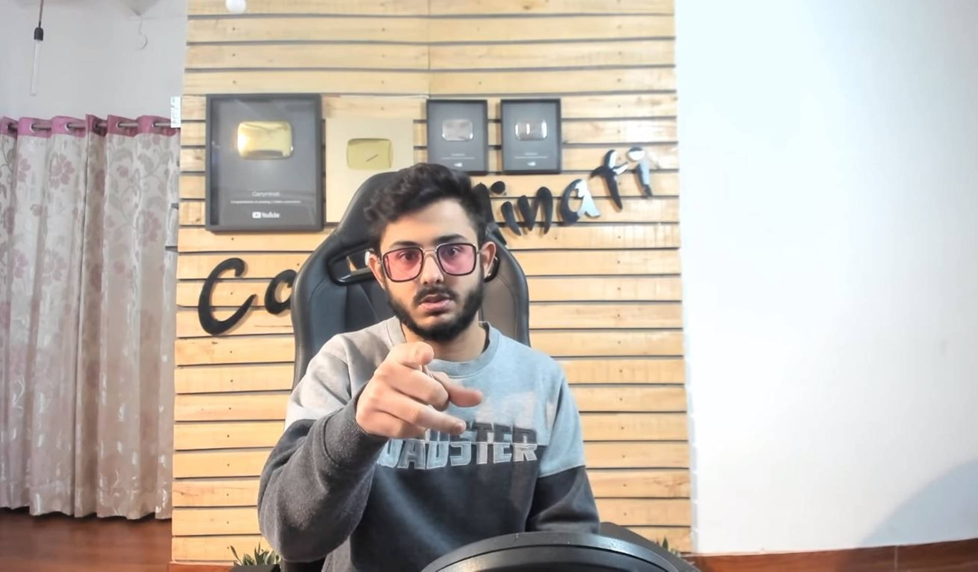 年輕男子坐在電競椅上指向相機，身後有YouTube獎項。