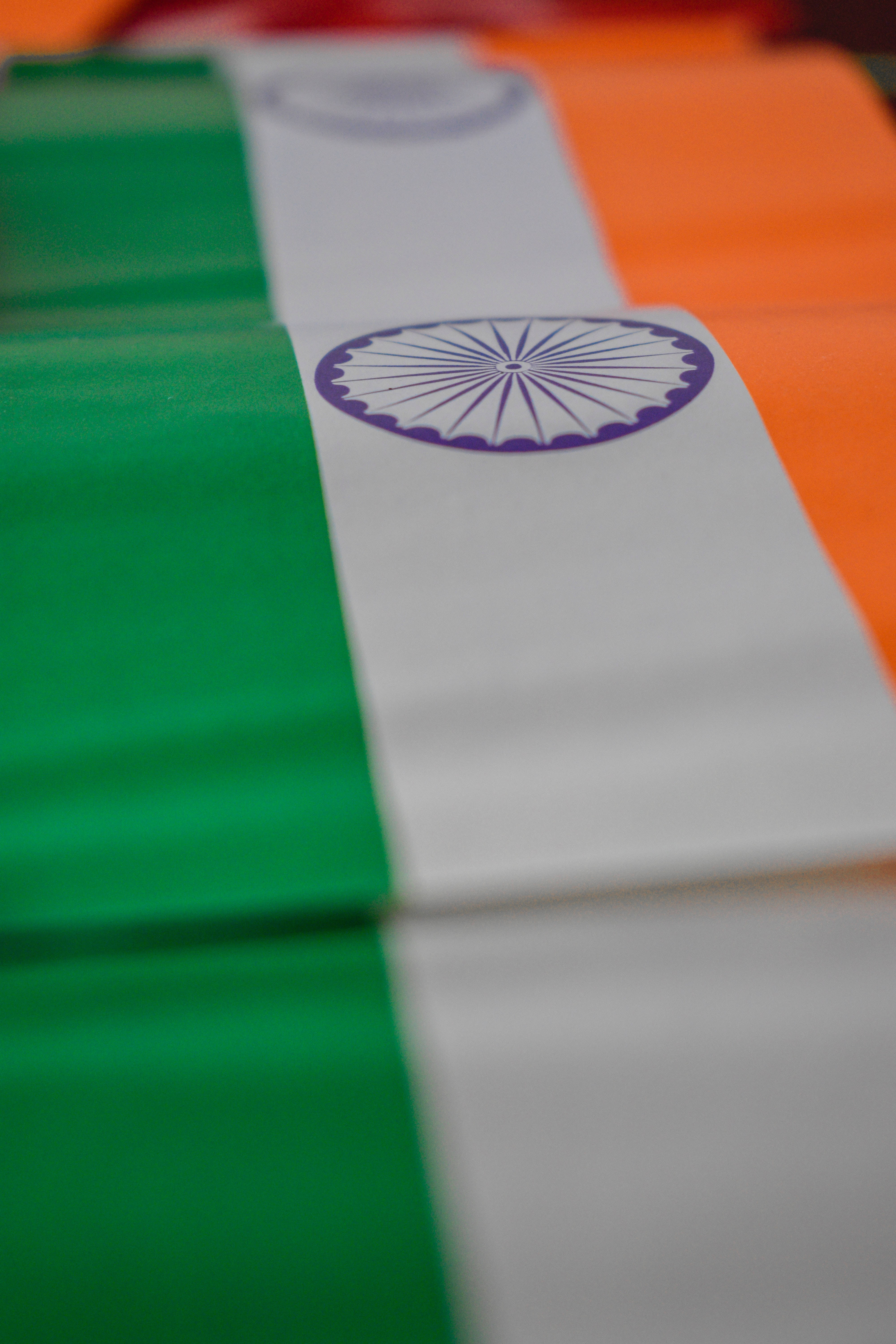 indian flag mobile 桌布 壁紙 — 印度三色旗的特寫，白色條紋中央有阿育王法輪，顯示布料摺疊和景深模糊效果。