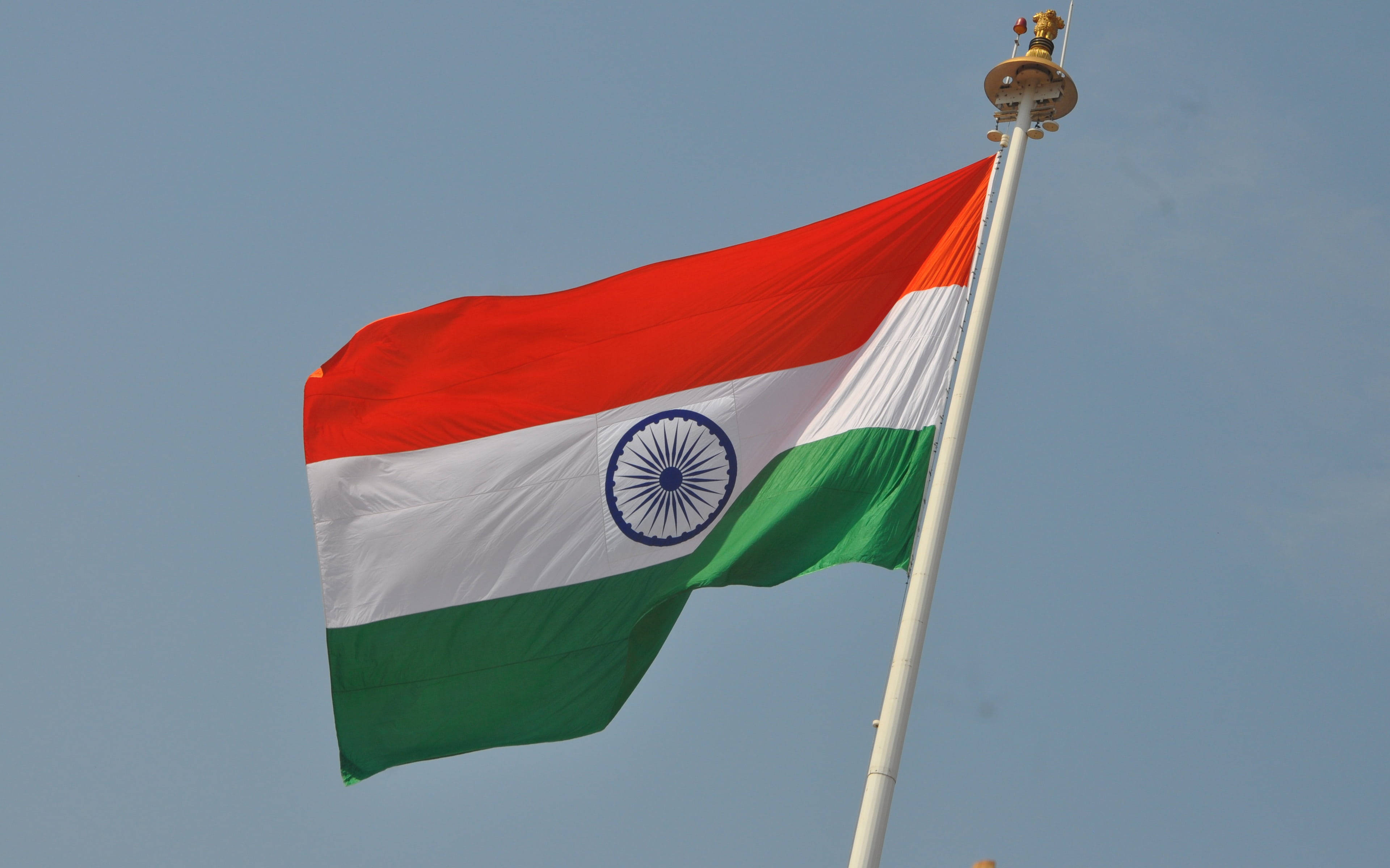 Indian 桌布 壁紙 — 印度國旗在清澈的藍天下自豪地飄揚，帶有藏紅花、白色和綠色條紋，以及中間的海軍藍阿育王法輪。