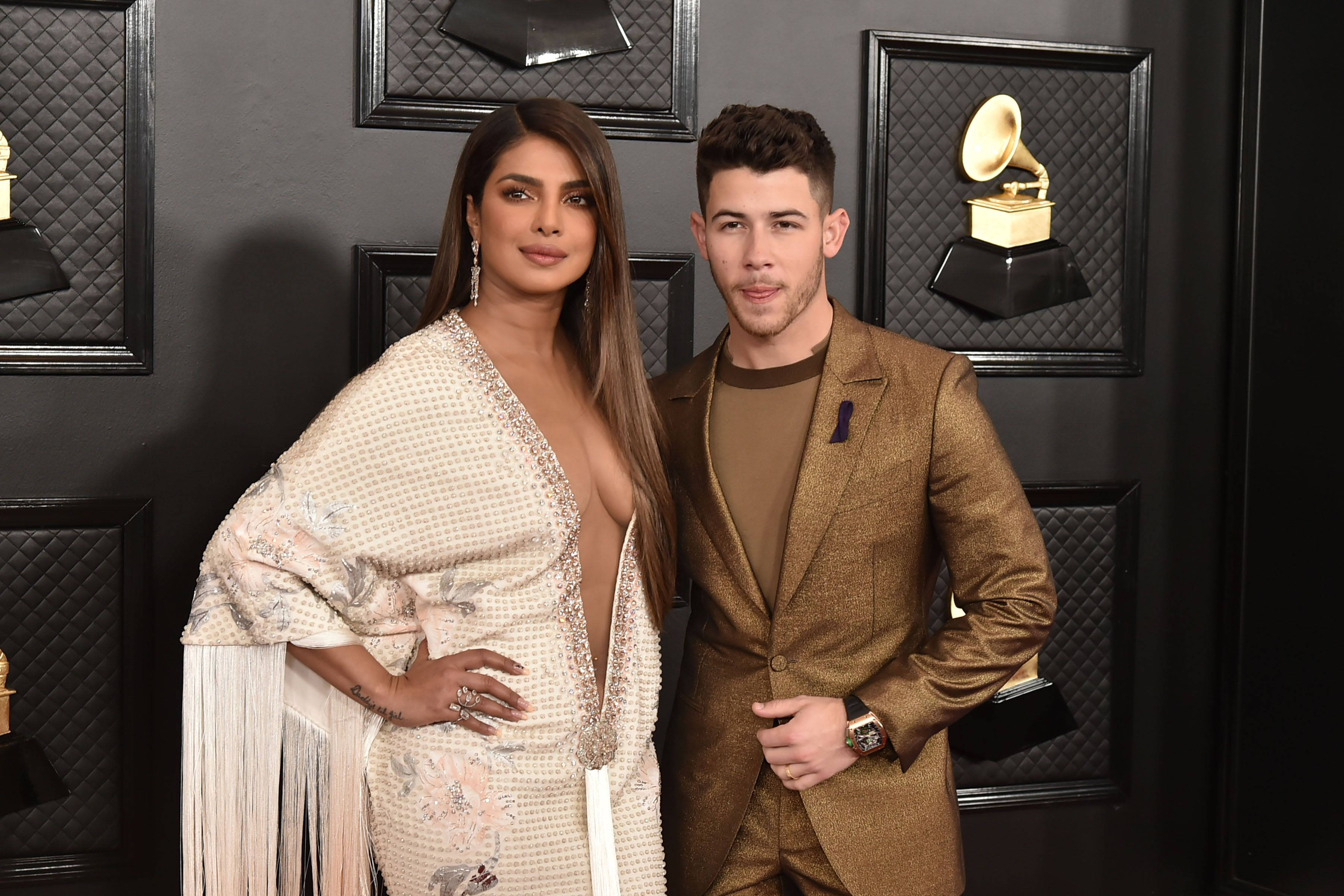 印度女演員普里揚卡·喬普拉與丈夫同框 壁紙 — Priyanka Chopra 和 Nick Jonas 在格林美獎上自信地擺姿勢，背景是裝飾著金色留聲機獎盃的黑牆。