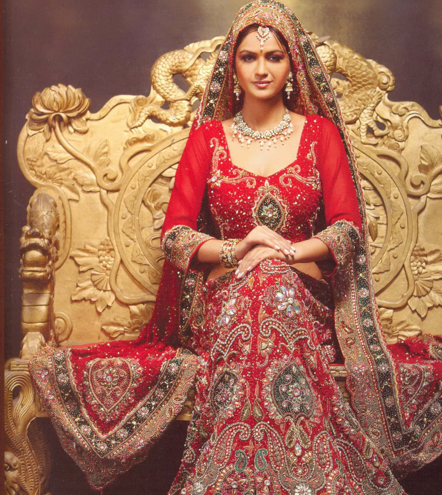 印度新娘坐金椅照片 壁紙 — 一位身穿華麗刺繡紅色新娘禮服（lehenga）的女性，端莊地坐在裝飾華麗的金色寶座上。