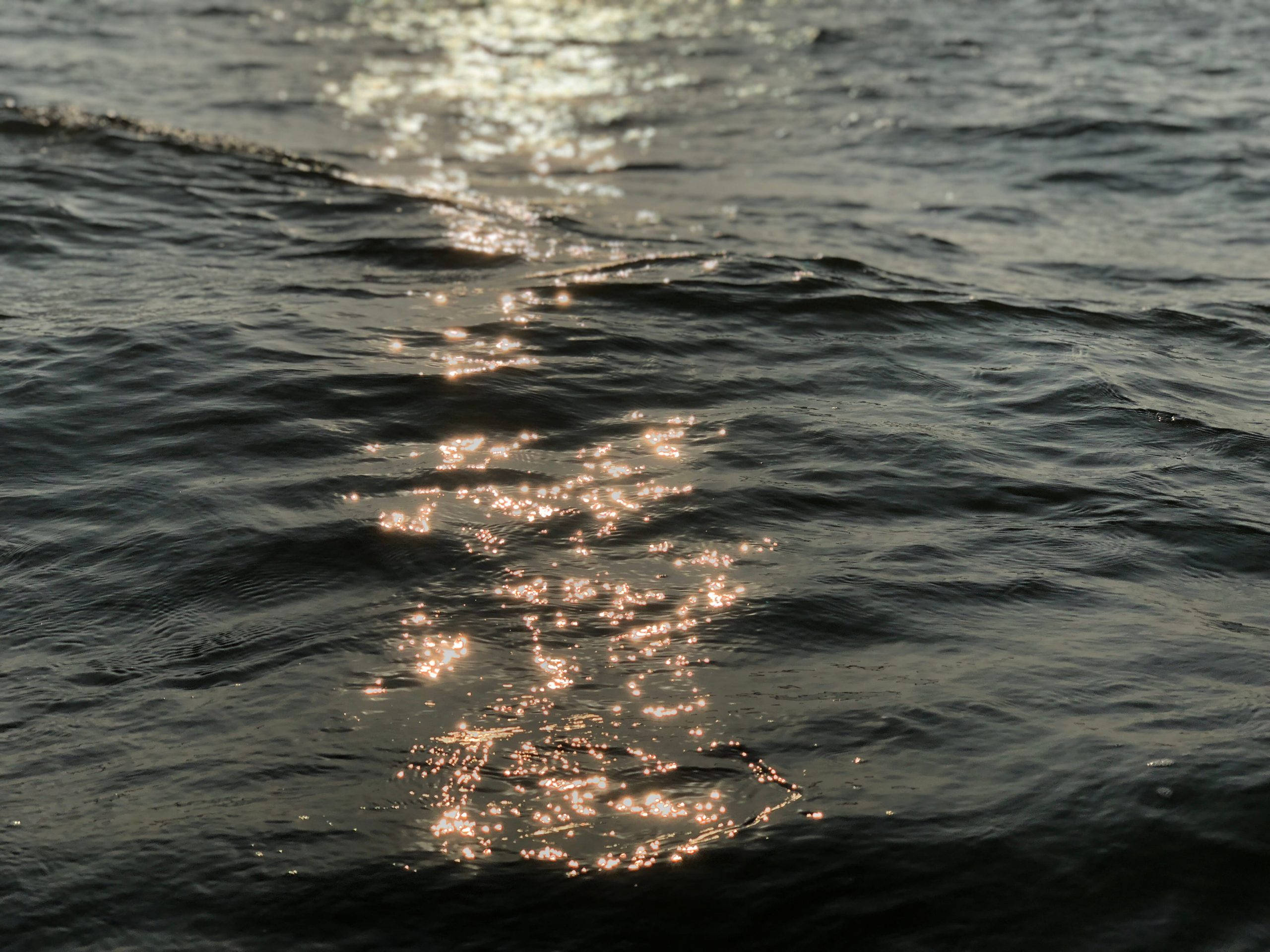 印度果阿海浪 壁紙 — 陽光照耀在黑暗的漣漪水面上，形成一條閃爍的金色火花路徑。