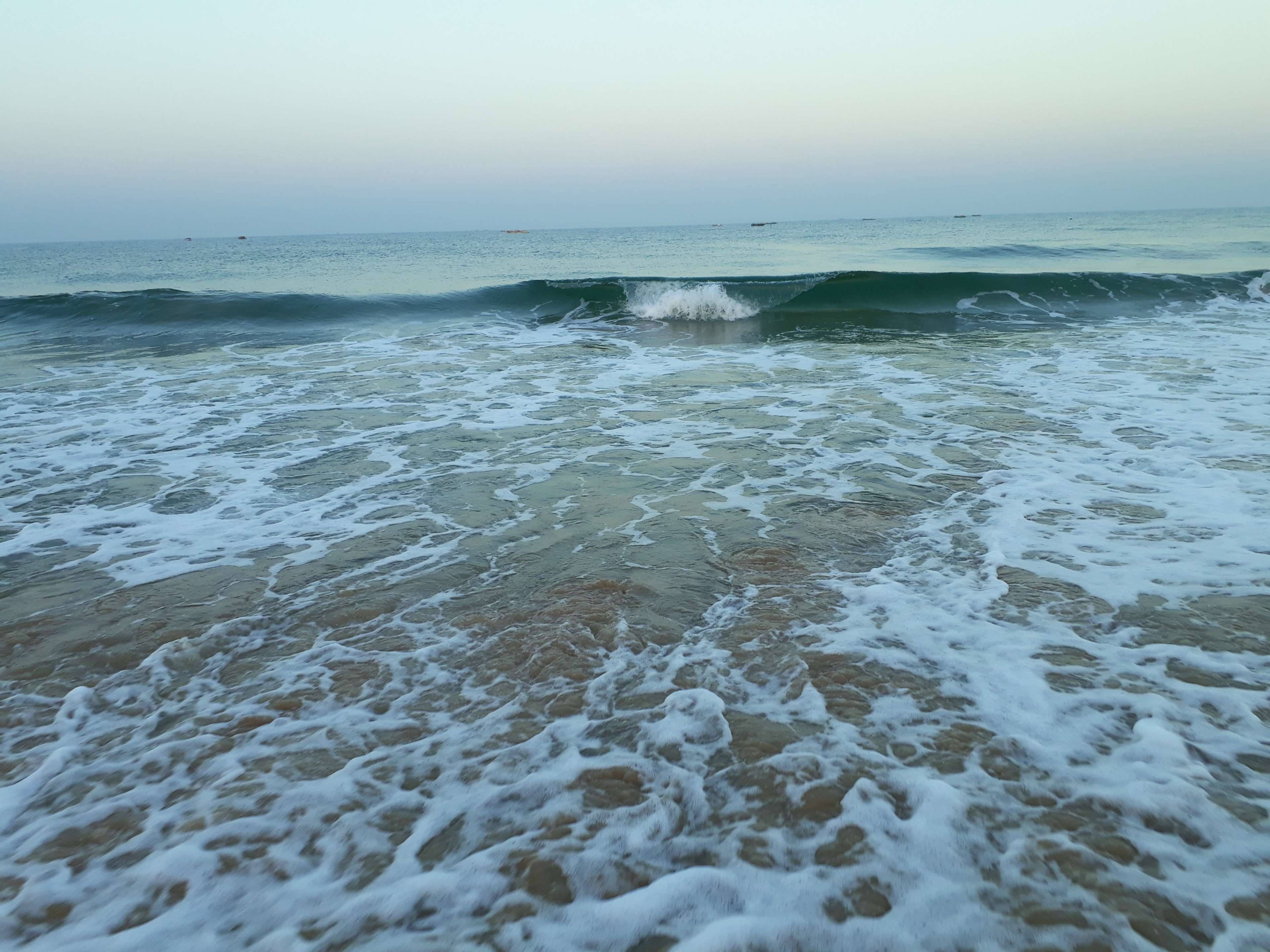 印度果阿海的壯麗下午景色 壁紙 — 泡沫海浪在柔和嘅暮色天空下翻滾到沙灘上。