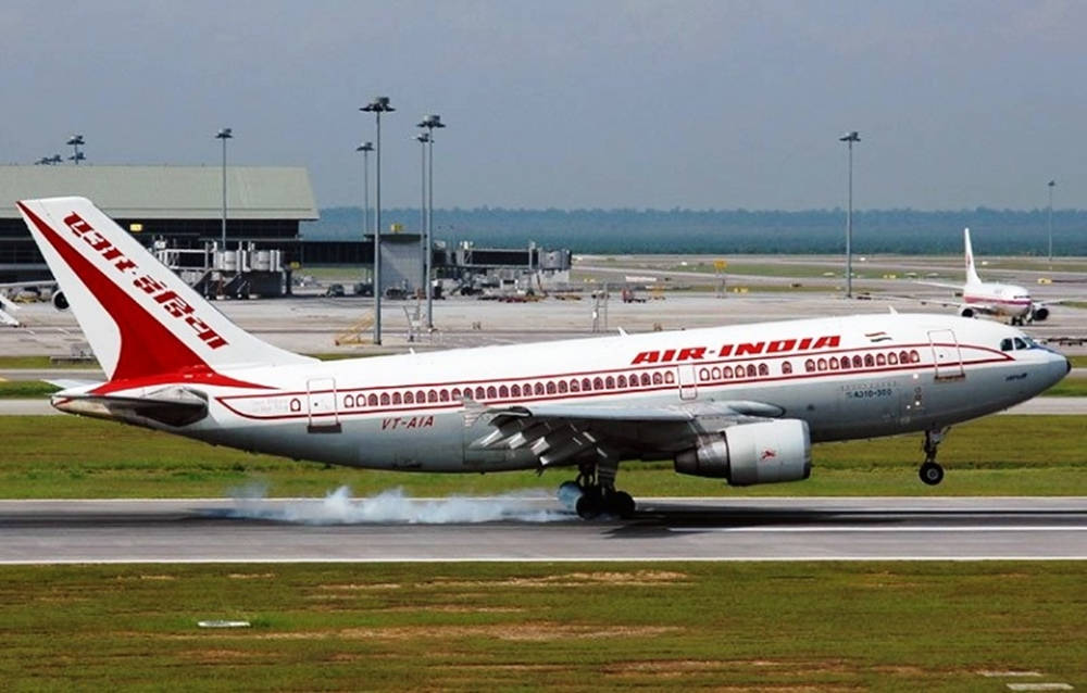 印度航空飛機在跑道上降落，背景有機場建築物和綠色山丘。