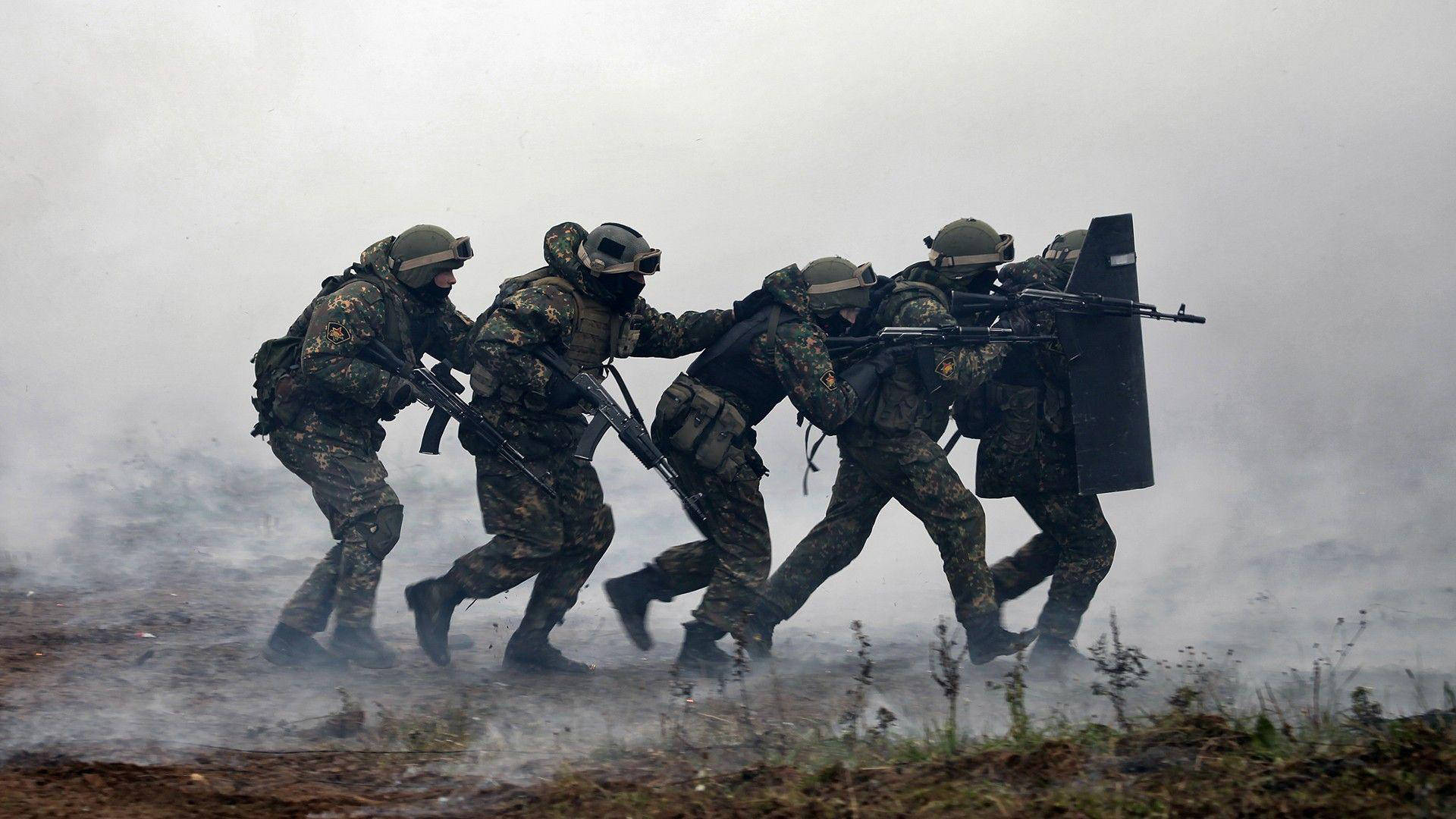 身穿迷彩裝備的士兵手持步槍和盾牌穿過煙霧前進。