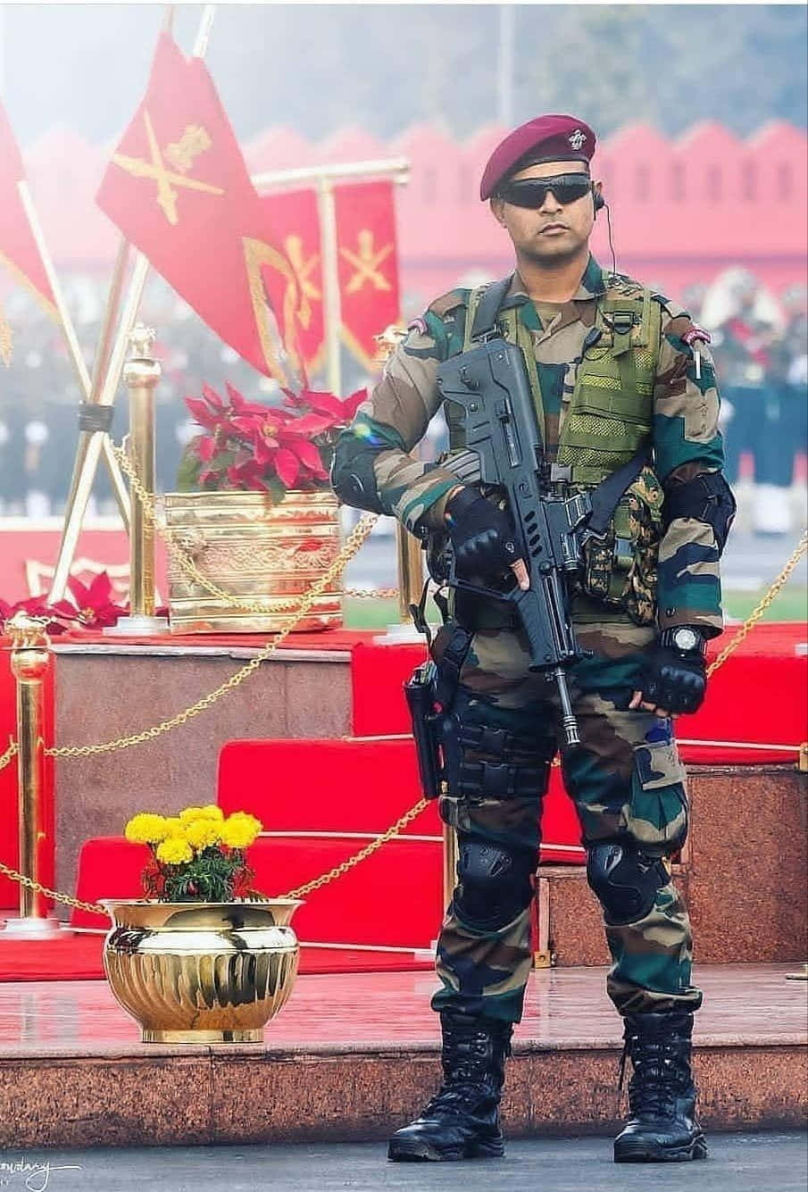 印度軍隊的力量與榮譽 壁紙 — 一名身穿迷彩服和紅色貝雷帽的士兵，在帶有金色花盆和旗幟的紅色台階旁持步槍立正站立。