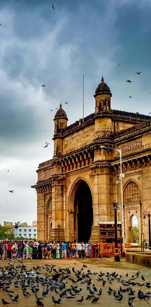 Gateway of India monument with pigeons and tourists under cloudy sky.