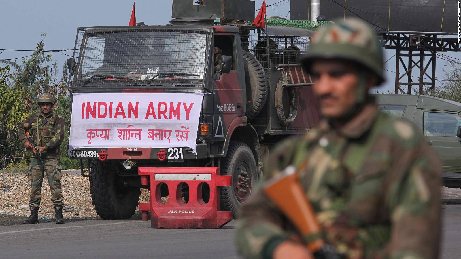 Indian Army 桌布 壁紙 — 印度陸軍士兵喺一架展示印地語文字橫額同紅色警方路障嘅軍車旁邊站崗。