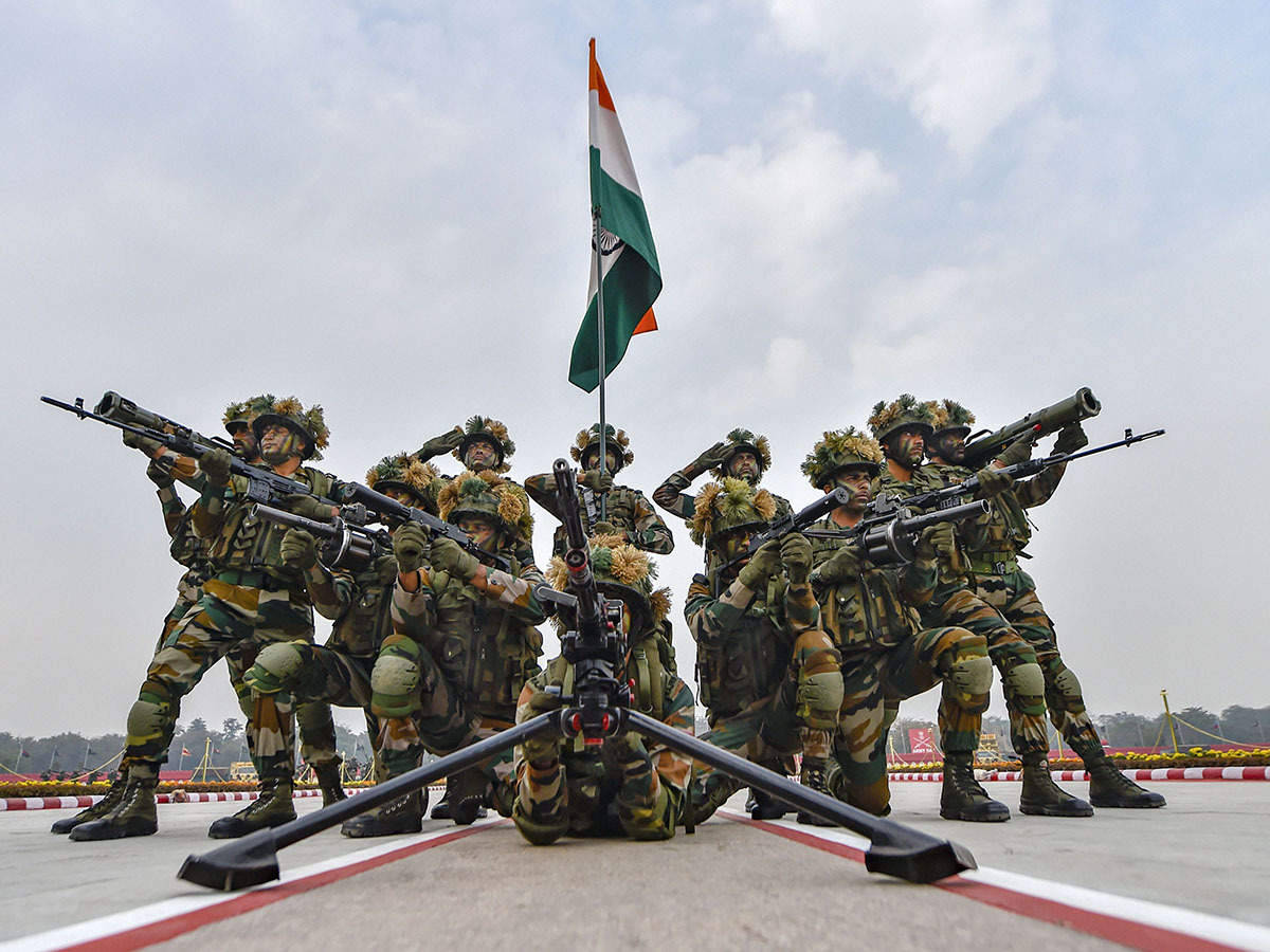 Indian Army 桌布 壁紙 — 印度陸軍士兵身穿迷彩服，在陰天持步槍立正，旁邊國旗飄揚。
