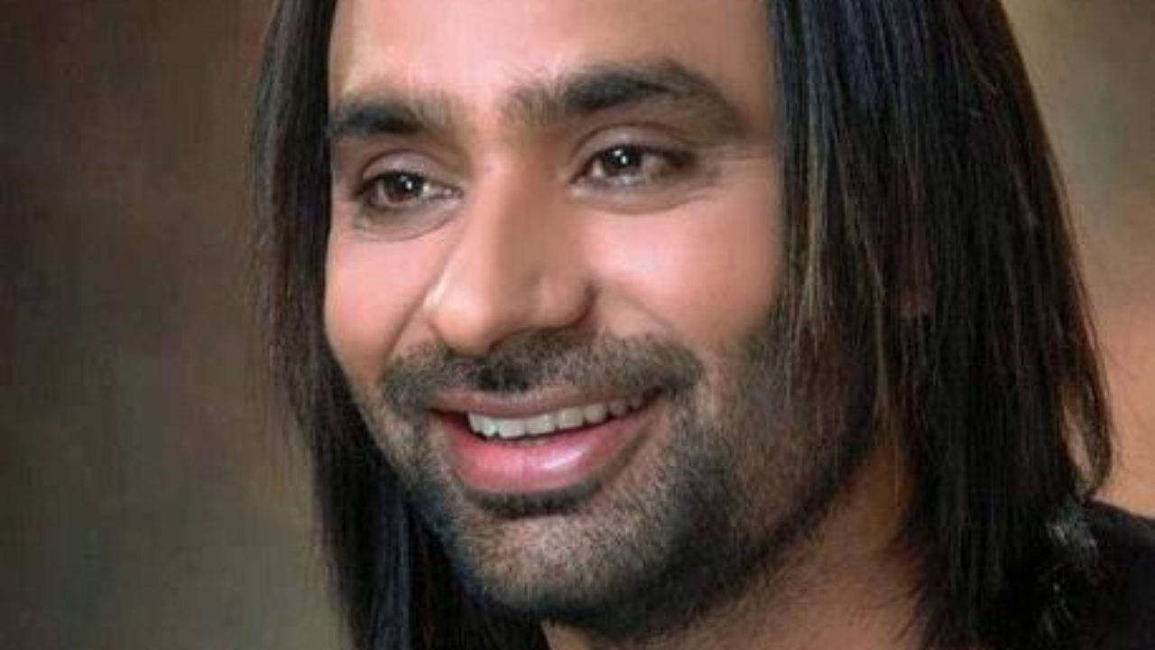 一個在工作室肖像中微笑的長黑髮、留鬍子的男士。