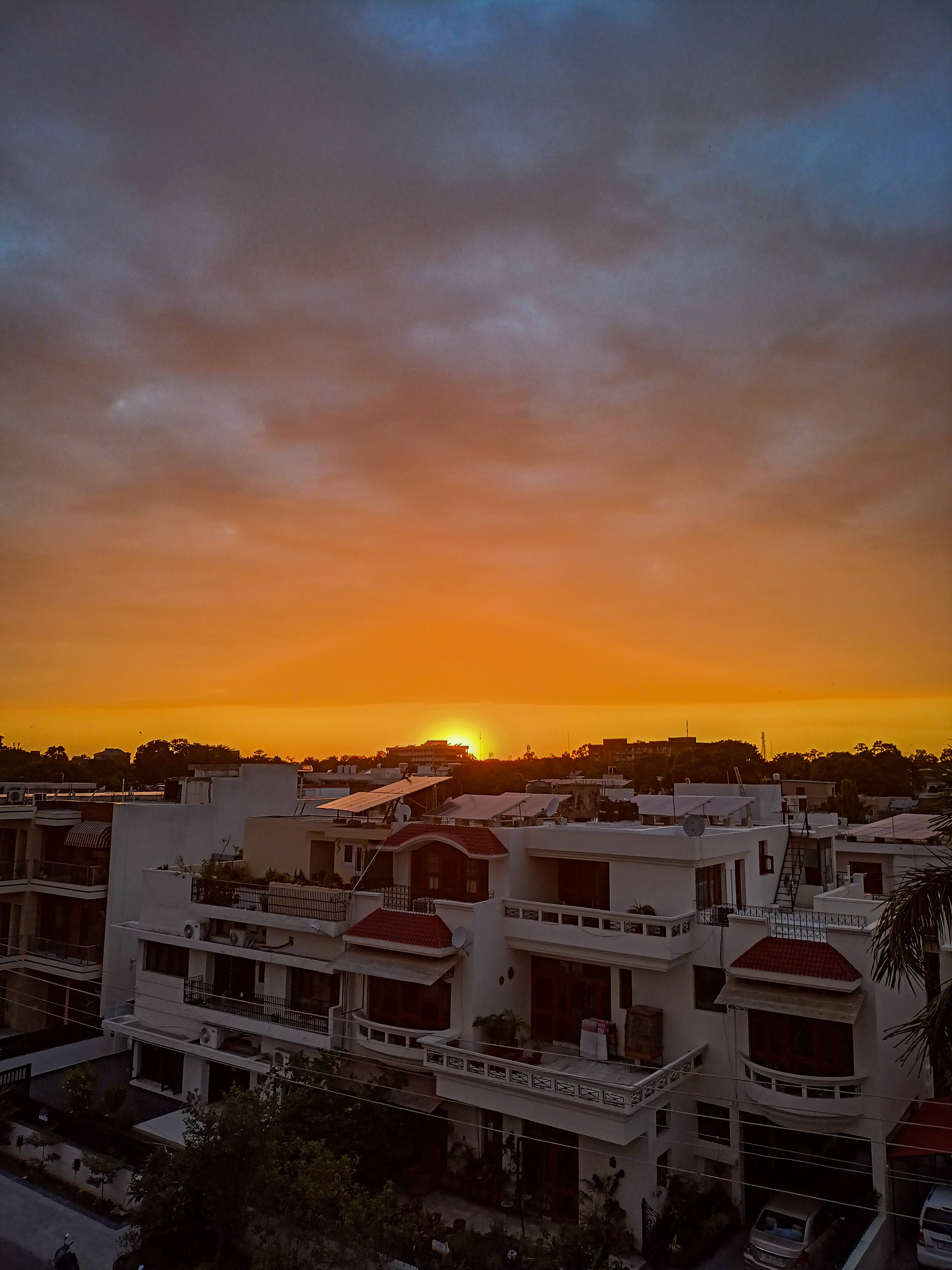 印度風夕陽 壁紙 — 夕陽將天空染成火橙色和深藍色，映照在白色住宅建築和紅色屋頂之上。