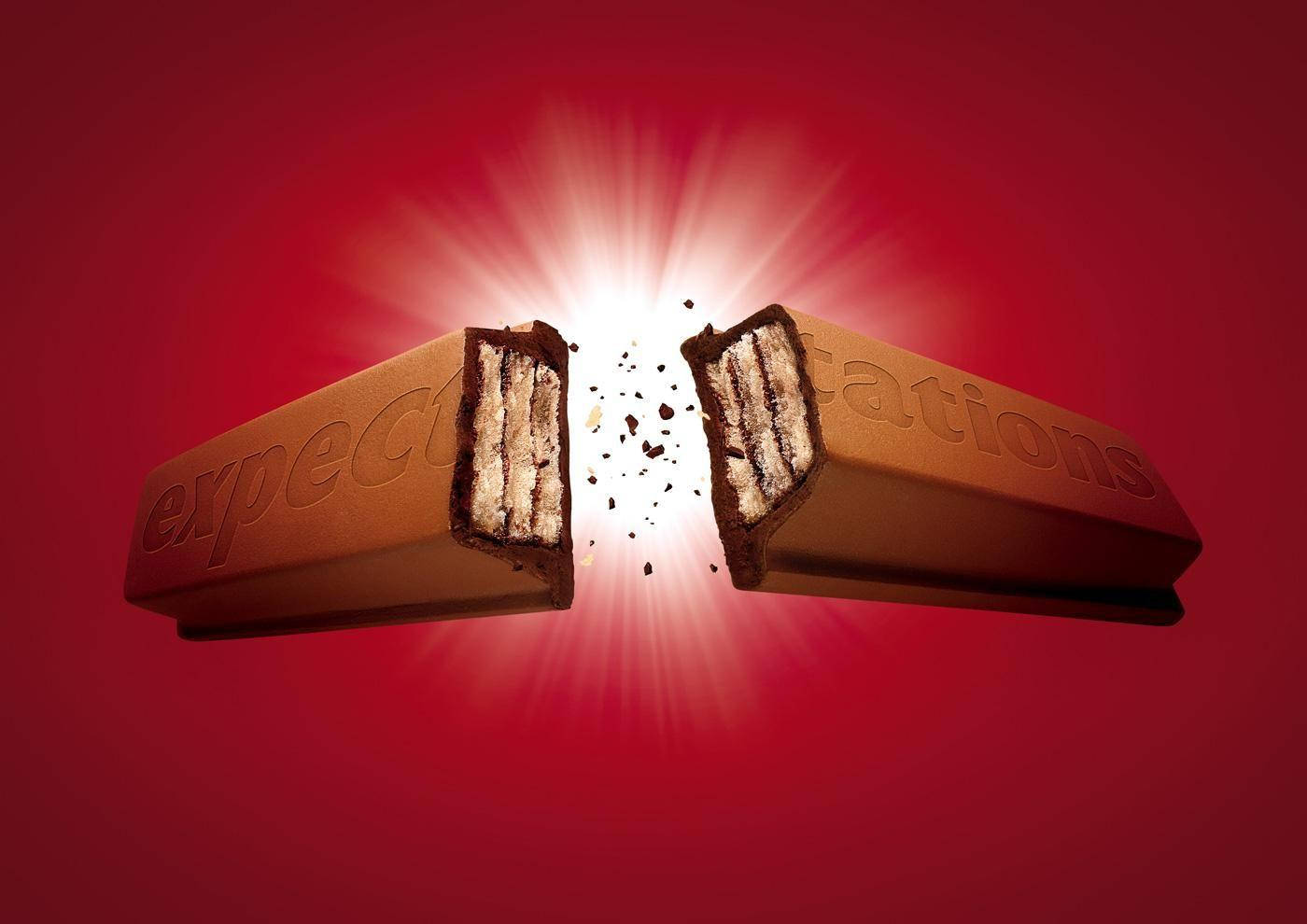 印有「Expectations」字樣的 Kit Kat 壁紙 — 一條朱古力棒從中間裂開，裂縫中迸發出明亮的光芒，背景為深紅色。