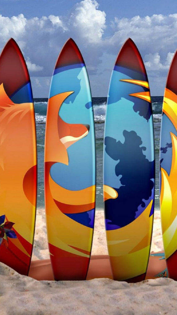 印有 Firefox 標誌的衝浪板海灘 iPhone 壁紙 — 充滿活力的衝浪板，帶有火熱的橙色、藍色和黃色抽象設計，直立於沙灘前景，背景是海浪和多雲的天空。
