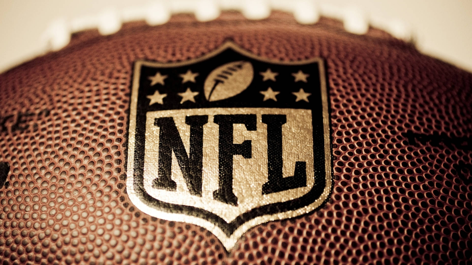 印有 NFL 標誌的足球 壁紙 — NFL標誌近距離特寫，縫在棕色皮革足球上，可見鞋帶和紋理表面。