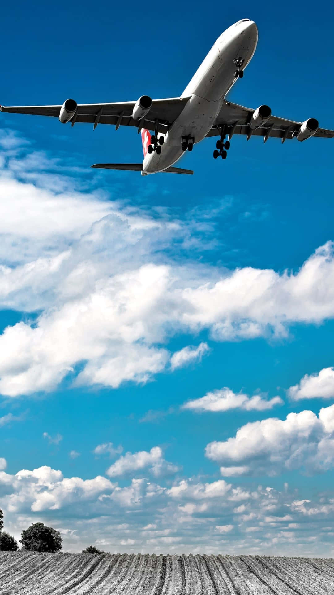 印有SWISS國際航空標誌的飛機安卓飛機壁紙 壁紙 — 一架大型客機放下起落架，在一片犁過的田野上空，對著充滿蓬鬆白雲的鮮豔藍天下降。