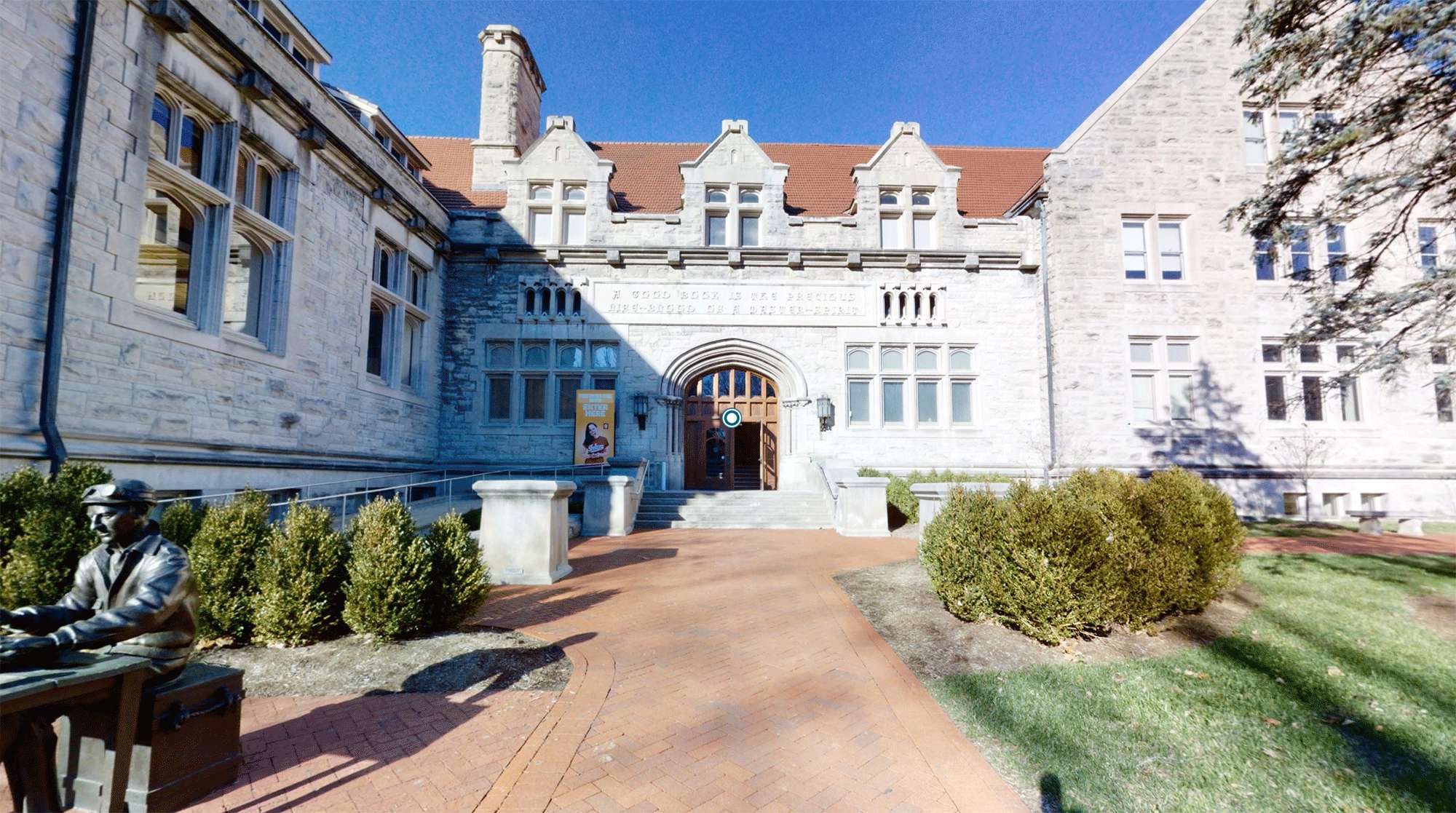 石造大學建築，有雕像和磚砌步道，在明亮陽光下。